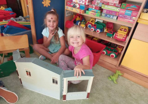 Dwie dziewczynki bawią się zabawkowym domkiem